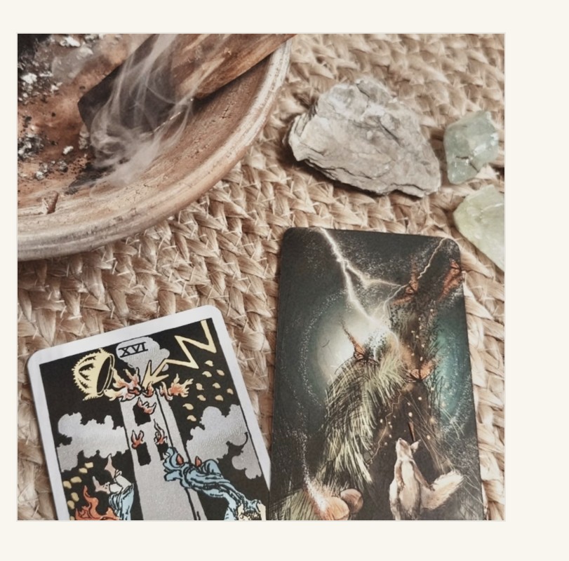 Tarot cards, crystals, and burning sage arranged on a woven mat